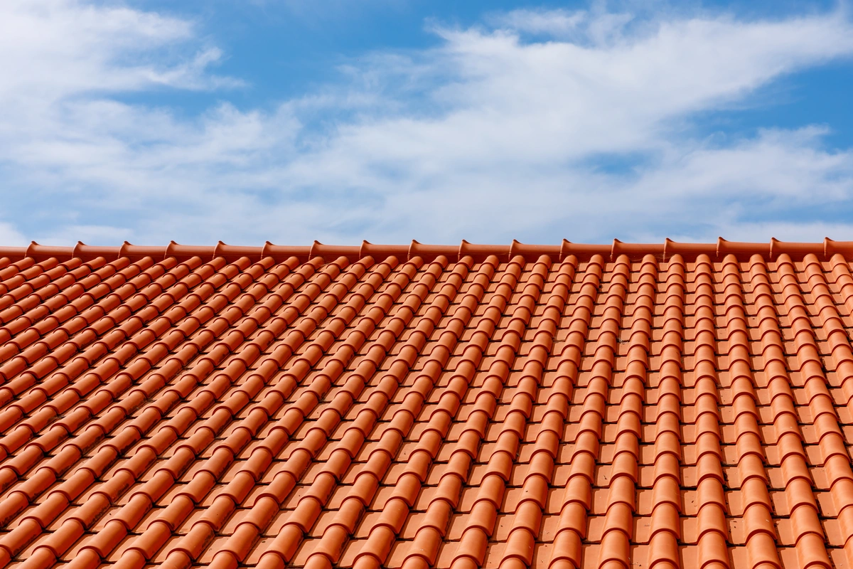 A close-up view of a Spanish tile roof made of red clay tiles set against a blue sky with scattered white clouds.