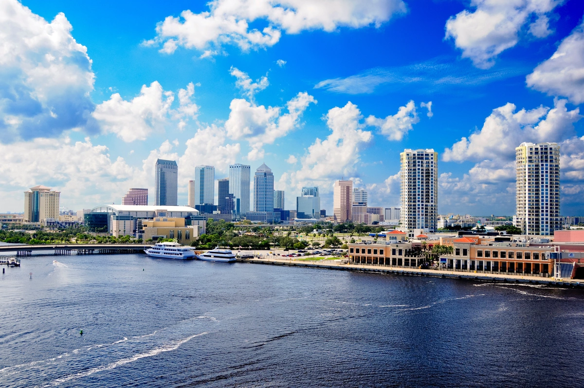 A vibrant city skyline with modern high-rise buildings and boats docked along a waterfront under a bright blue sky with scattered clouds—perfect for exploring things to do in Tampa with kids.