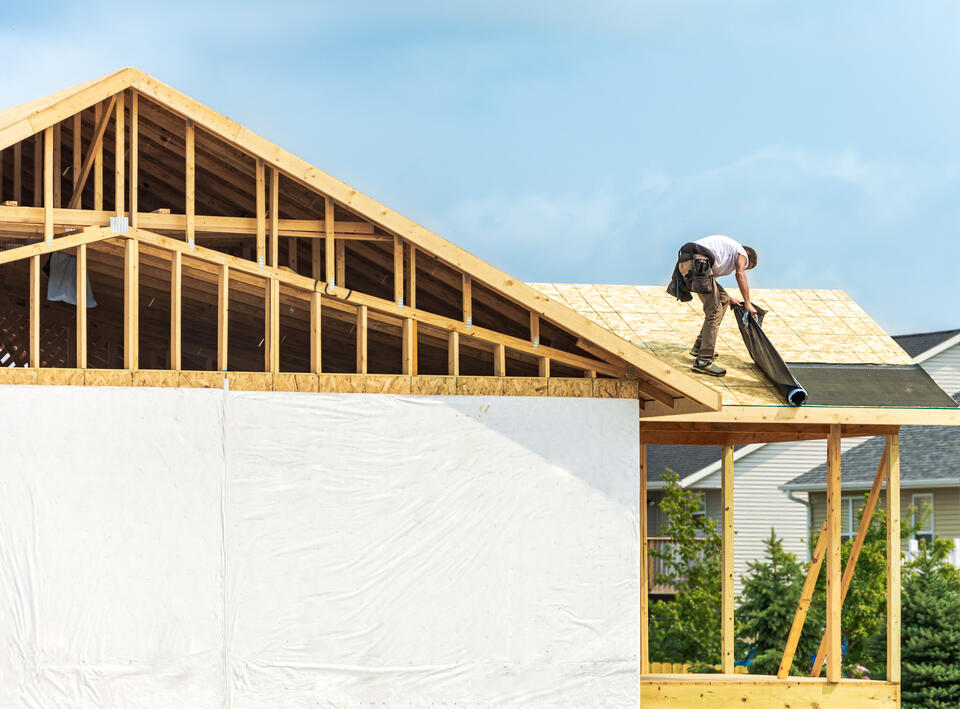 synthetic roof underlayment-man unrolling underlayment onto roof decking during house construction