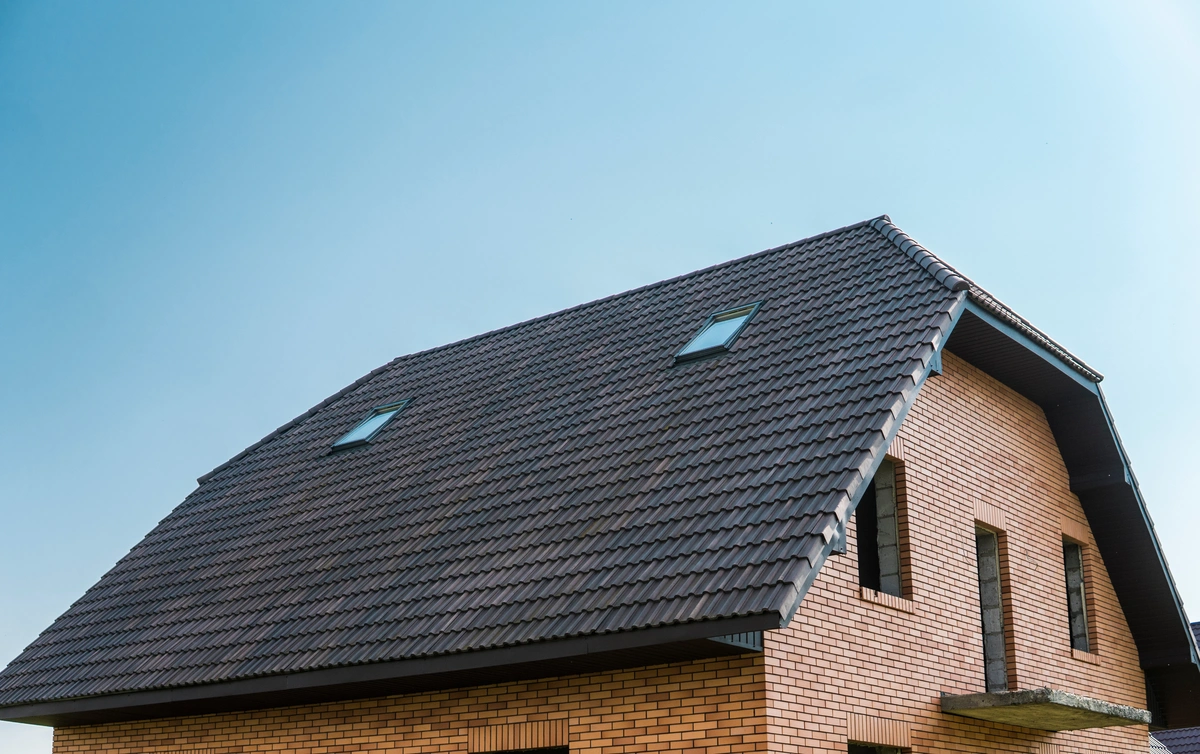 A close-up view of a modern brick house with a dark tiled sloped roof—highlighting the sleek finish possible with clay vs concrete roof tiles—and two skylight windows, set against a clear blue sky.