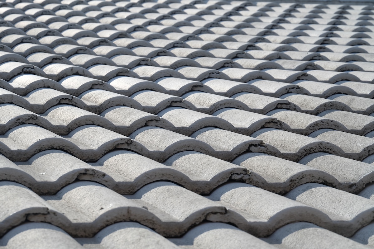 Close-up view of a tiled roof with overlapping, curved, gray ceramic tiles arranged in neat rows under natural light, offering a look at popular roof tiles types and prices for modern homes.
