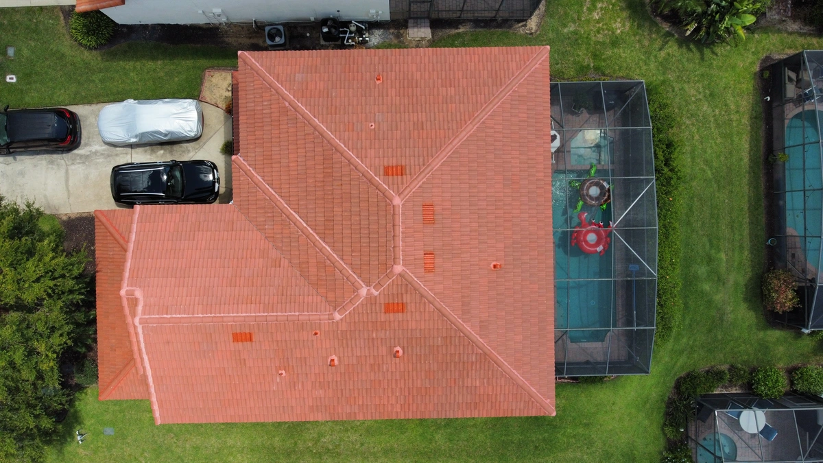 Aerial view of a house with a red tile roof, a driveway with two parked cars, and a screened backyard pool area. This charming property in roofing Riverview is surrounded by green lawns and neighboring homes.