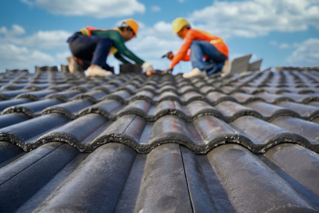 Select the focus on roof tiles. Blurred background of a roofer working on the roof of a house Use a drill to drill the screws to fix the cement tiles.