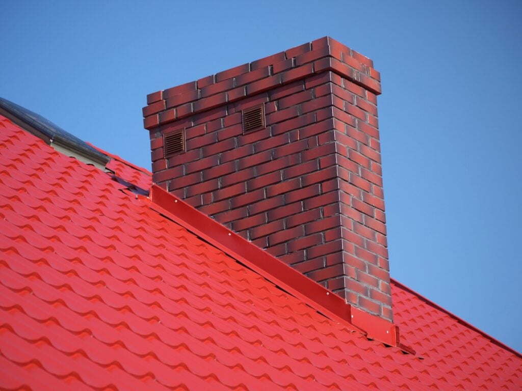 Closeup of red roof metal covering with brick chimney