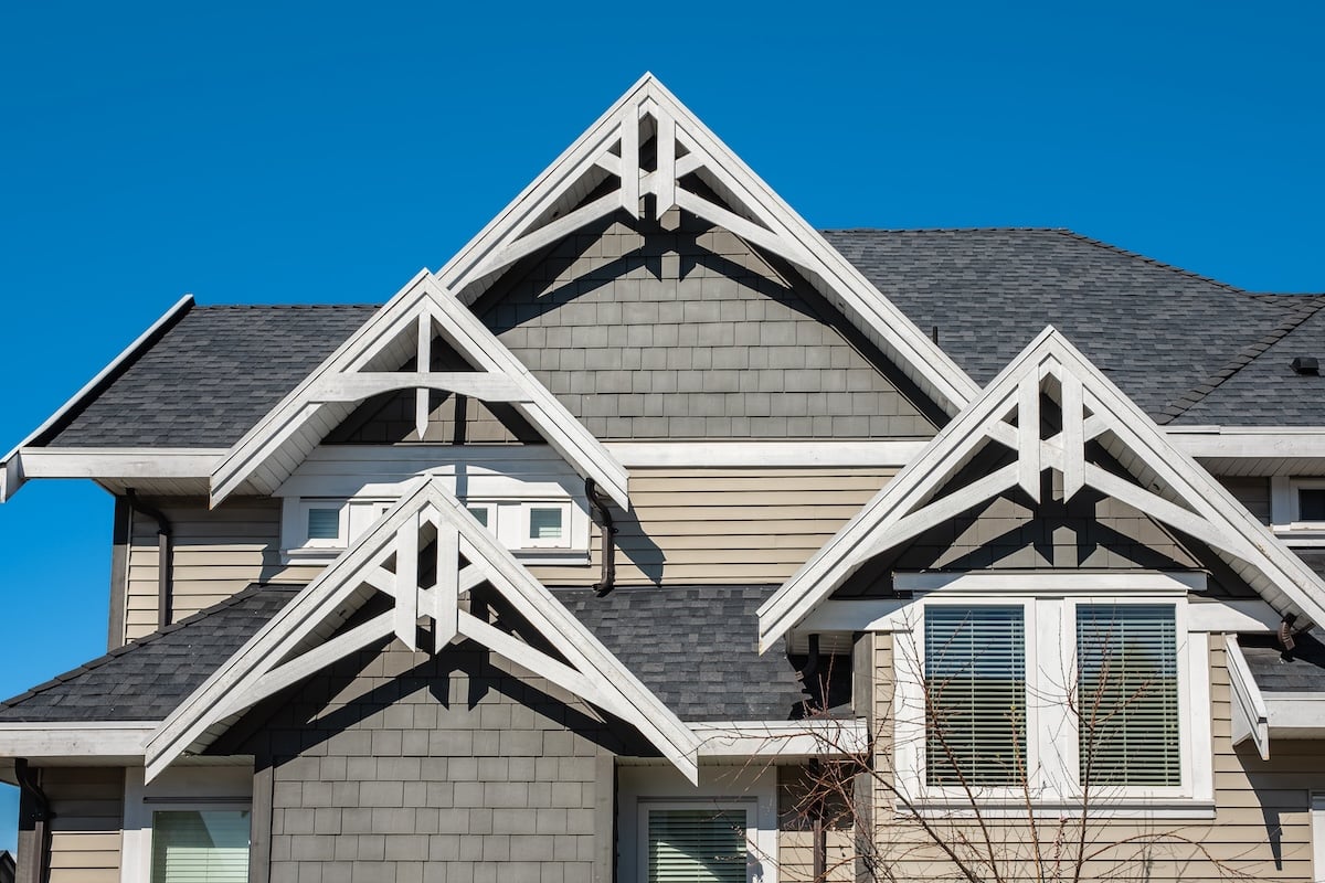 Close-up of a modern house exterior with three peaked gables, grey siding, white trim, and multiple windows—showcasing expert roofing Ruskin style—set against a clear blue sky.