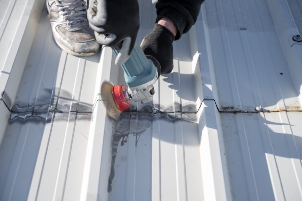 Man removing rust from white metal roof with grinding tool. Man holding grinder. Roof maintenance. Rust removal.