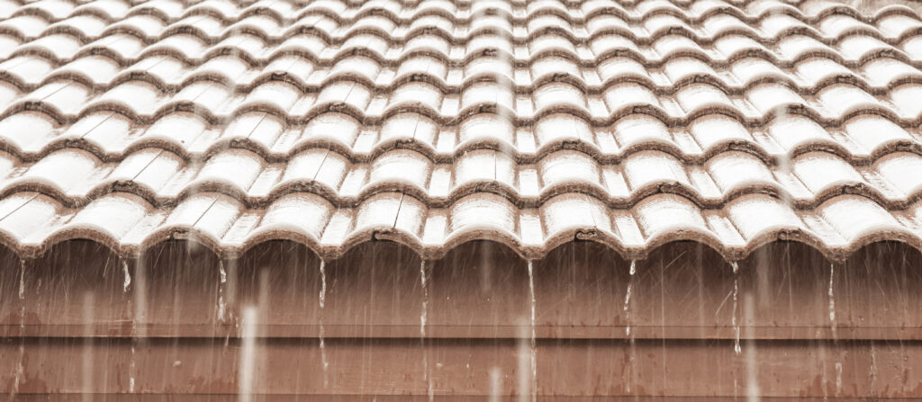 hurricane prep for roofs Wesley chapel Rainwater pours off a wavy, tiled roof, creating streams along the edges. The neatly arranged tiles highlight the importance of hurricane prep for roofs in Wesley Chapel, keeping homes safe even during heavy storms.