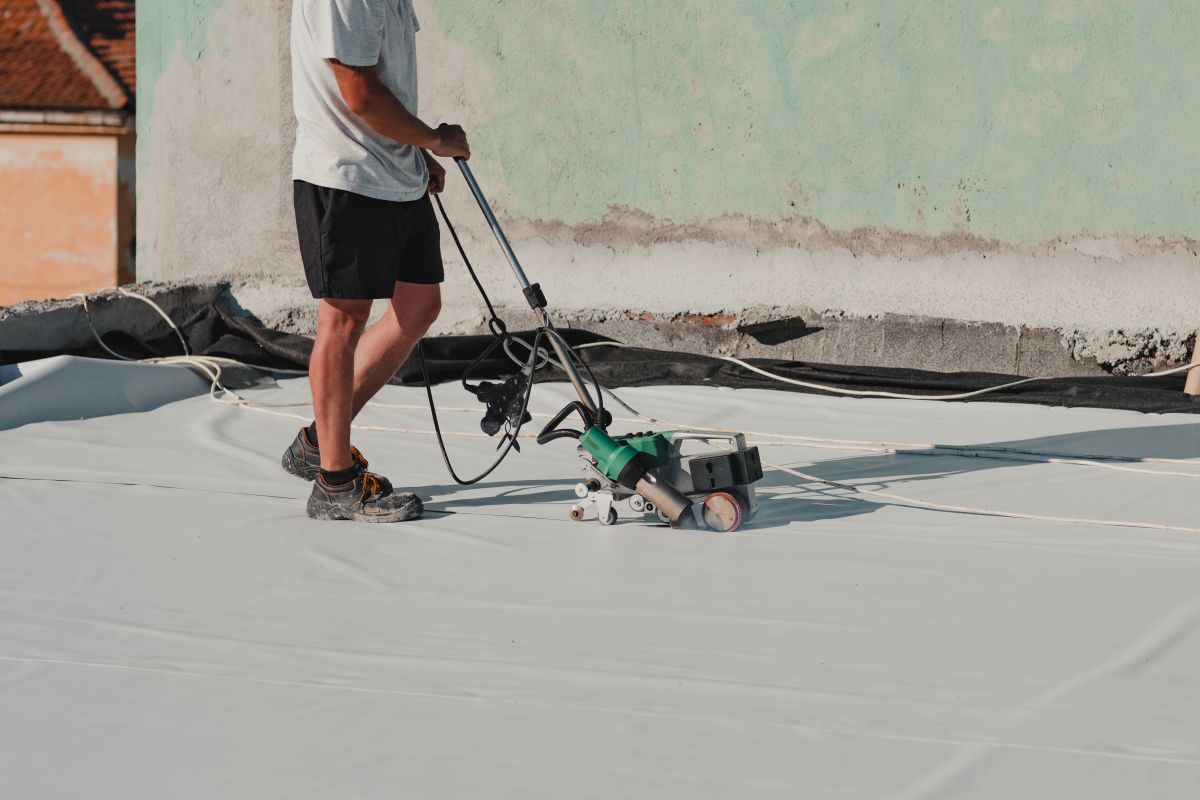 tpo roofing installation technician sealing floor with heater machine on top of commercial building