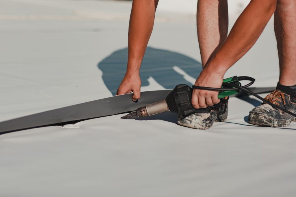 tpo roofing installation worker with dirty shoes using heater gun commercial building